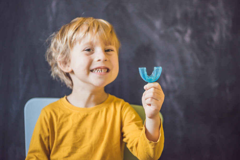 Three-year old boy shows myofunctional trainer. Helps equalize the growing teeth and correct bite, develop mouth breathing habit. Corrects the position of the tongue